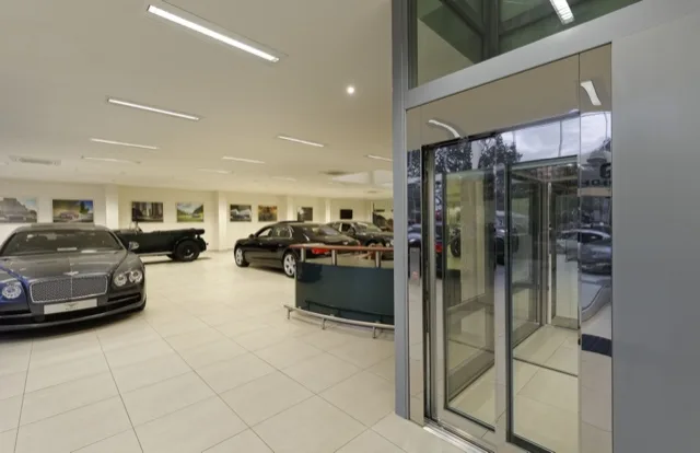 Panoramic glass elevator in a bright hall with classic cars