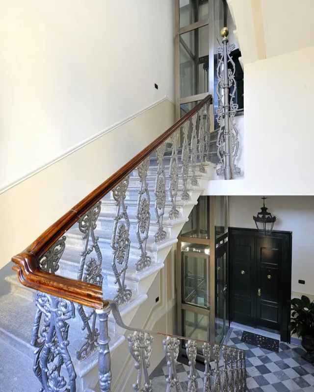 Glass elevator rising through a classic stairwell with an iron balustrade