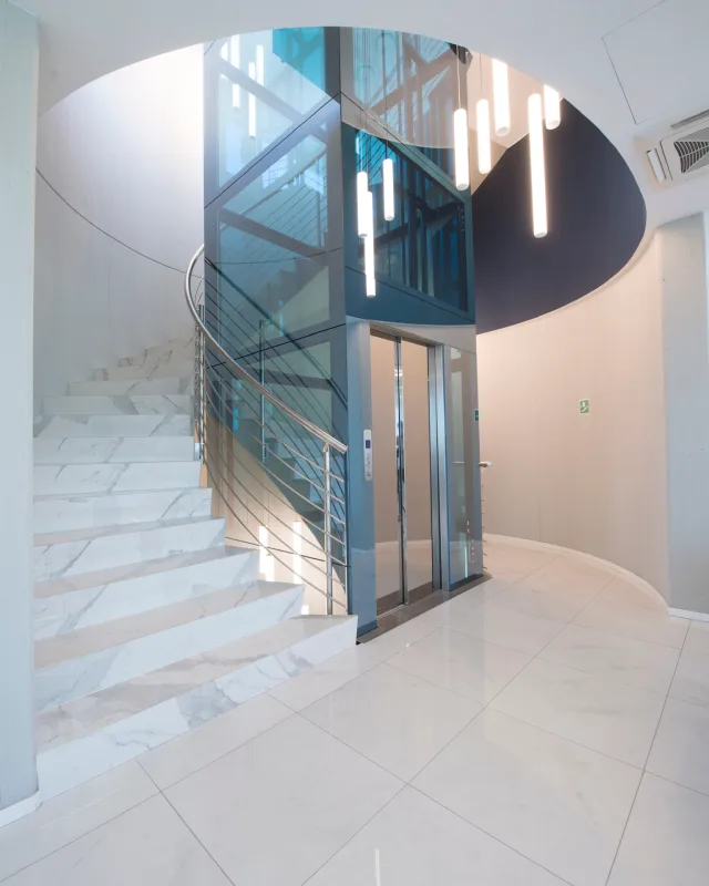 Glass elevator shaft rising inside a curved marble staircase
