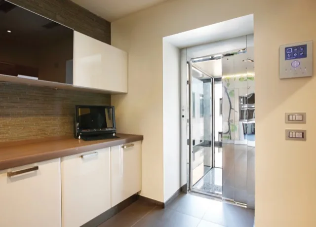 Glass elevator opening onto a kitchen with cream cabinets