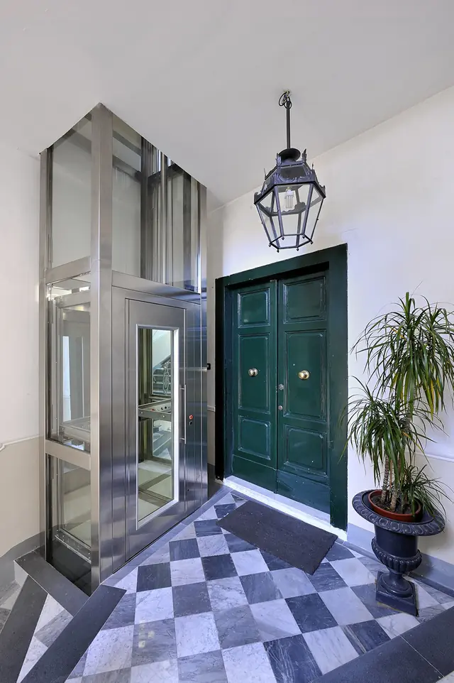 Stainless steel and glass elevator in an entrance hall with a checkerboard marble floor