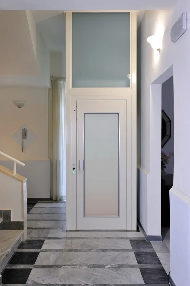 White elevator with a frosted glass door in a hall with a marble floor