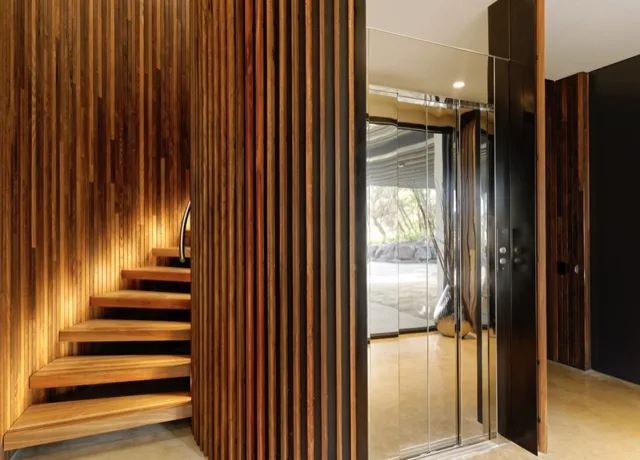Elevator beside a staircase clad in vertical wood slats