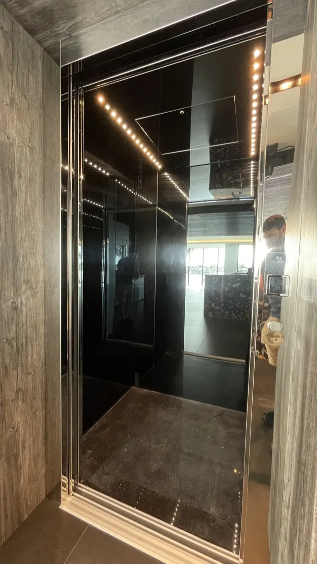 Elevator cab with black mirror walls, polished steel trim and rows of small ceiling lights