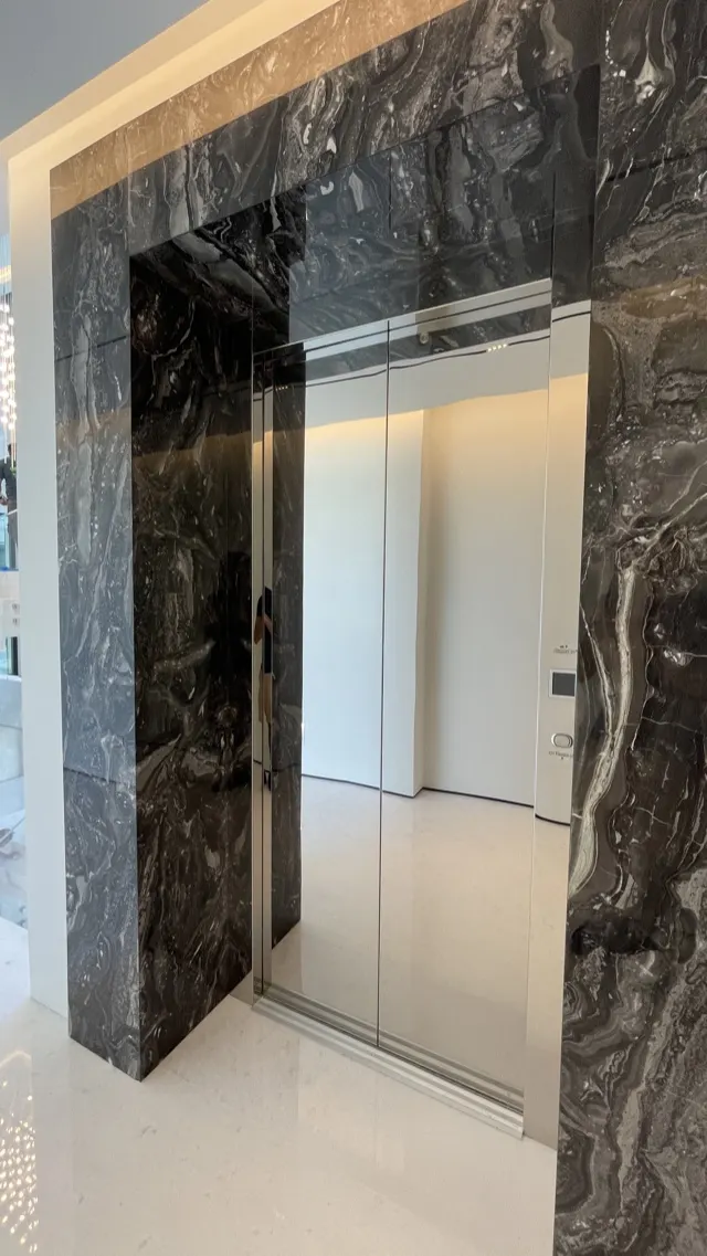 Polished stainless steel elevator doors set in a black marble portal