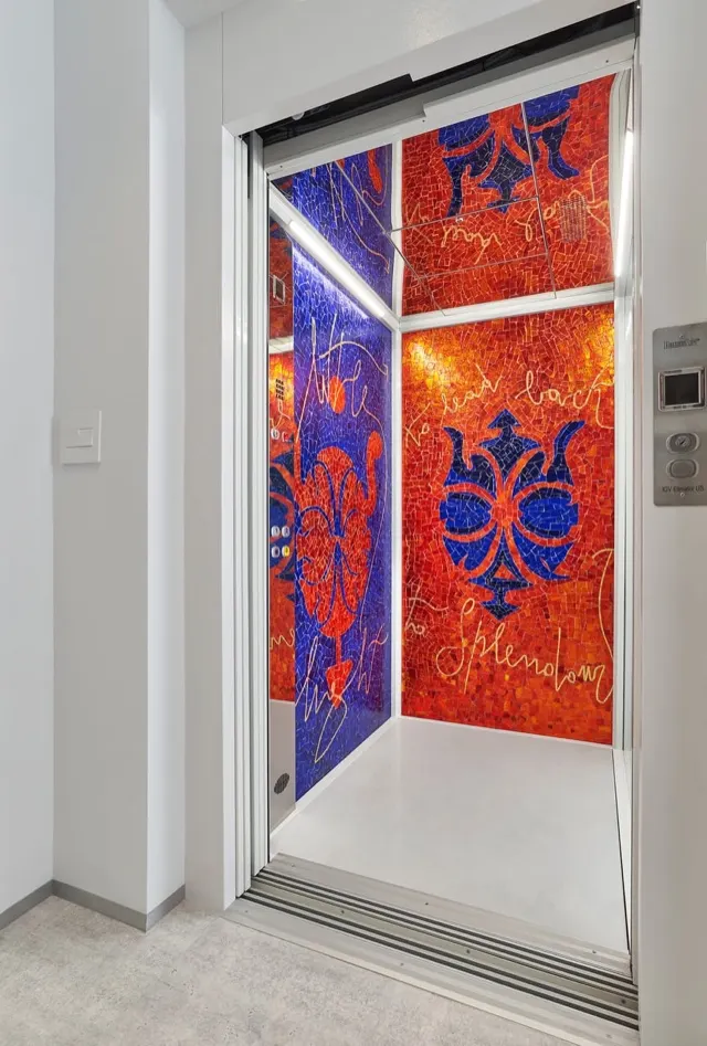 Open elevator cab with red and blue mosaic walls and a white floor