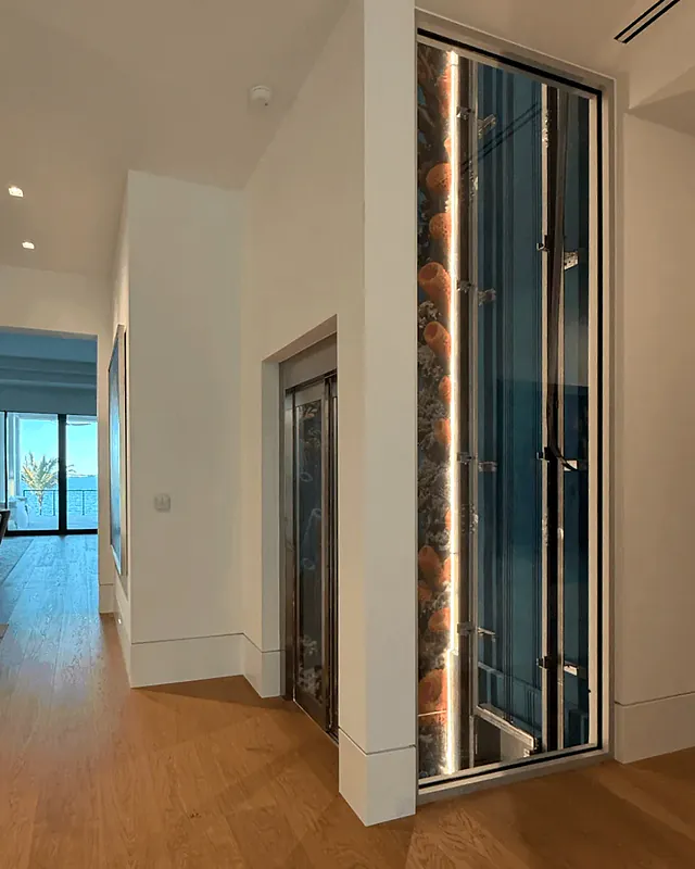 Illuminated, glass-fronted elevator shaft beside a white hallway